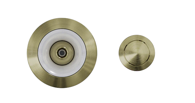 Two round metallic objects with a brushed brass finish. The left object is larger with a circular white rim and central point, resembling the Custom Nozzle Color for recessed ceiling lights or sprinkler heads. The right object is smaller, featuring a simple, smooth surface.