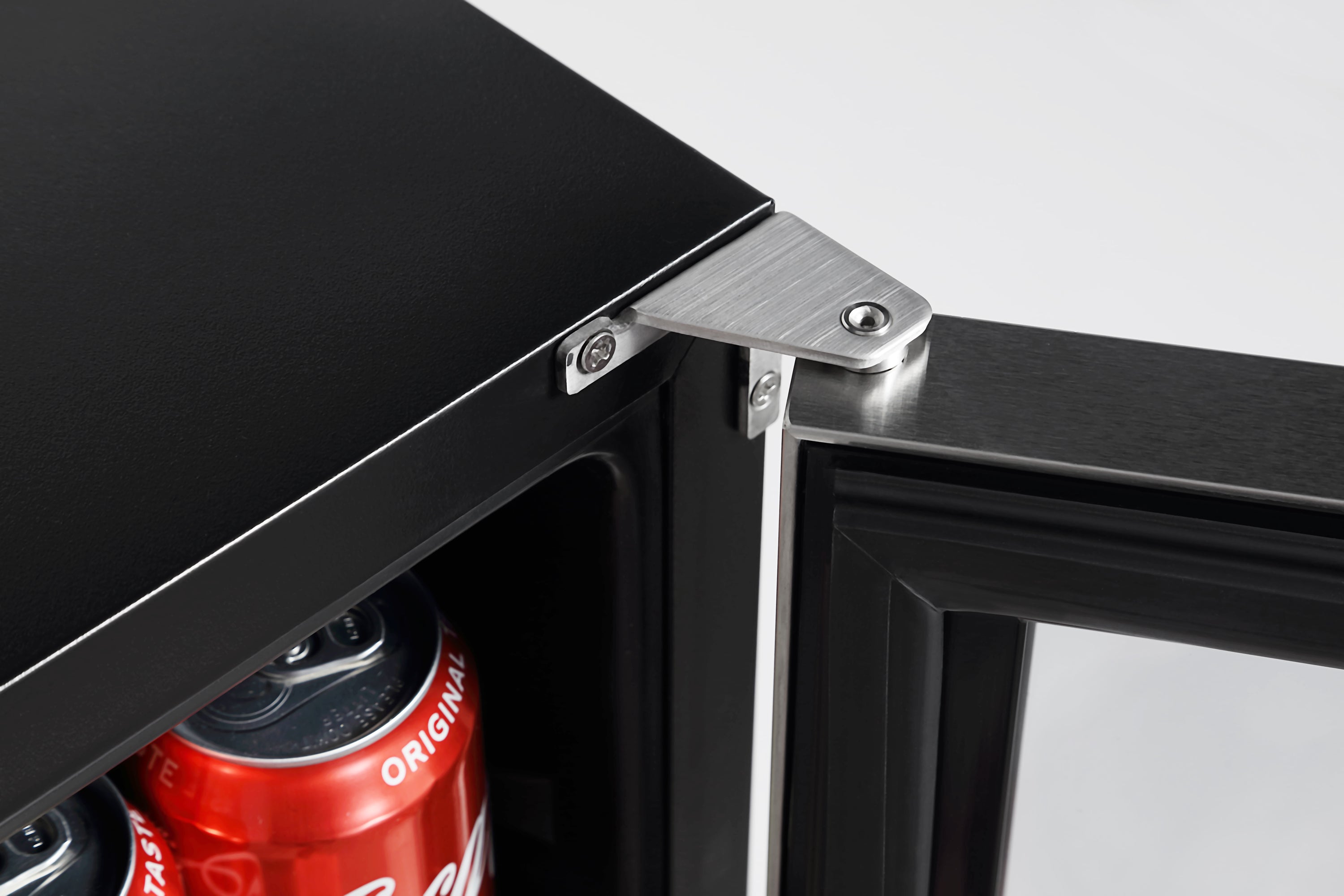 A close-up of a partially open black Empava 24 Inch Freestanding & Under Counter Beverage Fridge door, showcasing its hinge mechanism. Inside the appliance, there are cans of Coca-Cola, with part of the top can and another below it visible. The background is plain and white.