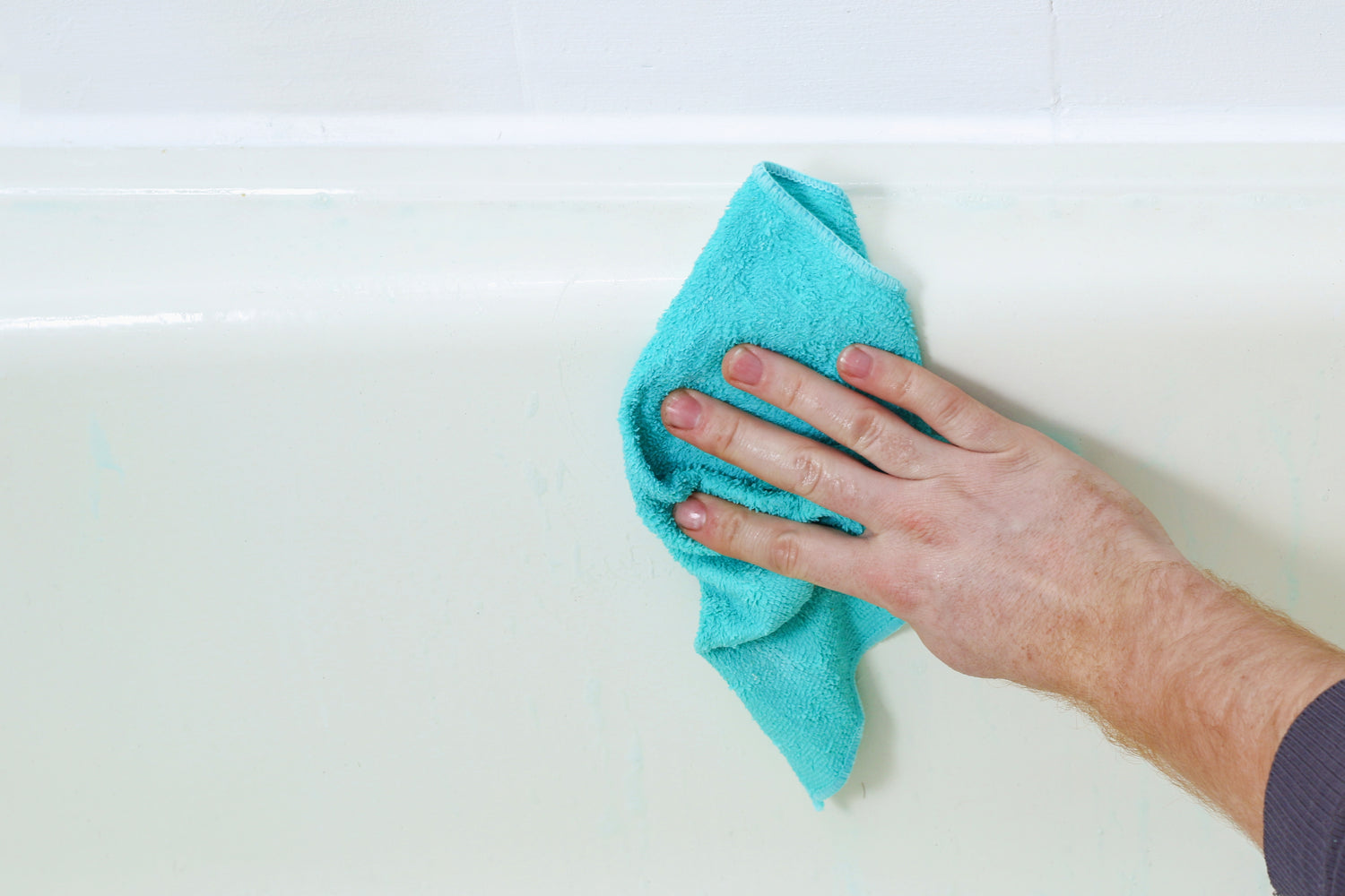 Person wiping down a tub with a blue cloth