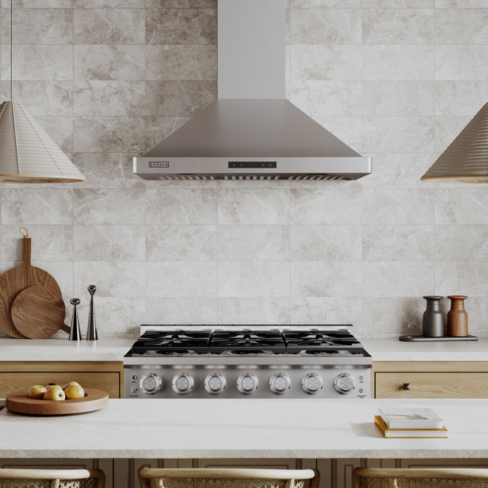 A modern kitchen with a stainless-steel stove and range hood. The backsplash features light-colored tiles. The countertop has wooden cutting boards, salt and pepper shakers, bowls of fruit, and other kitchen items.