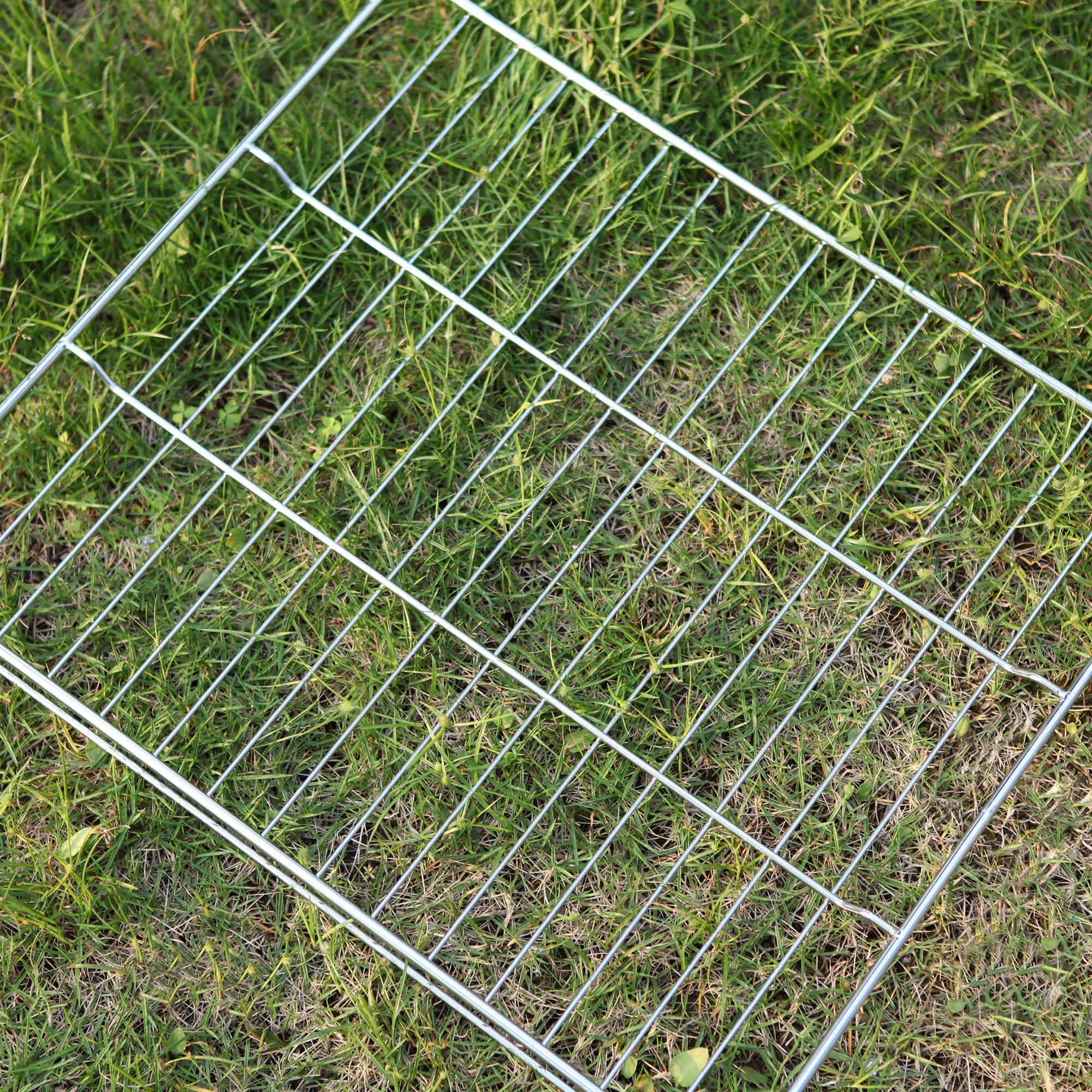 An Empava 24 Inch Wall Oven Rack with evenly spaced horizontal and vertical bars is positioned on the grass. The rack is slightly tilted, and its reflective surface creates a striking contrast with the green grass beneath it.