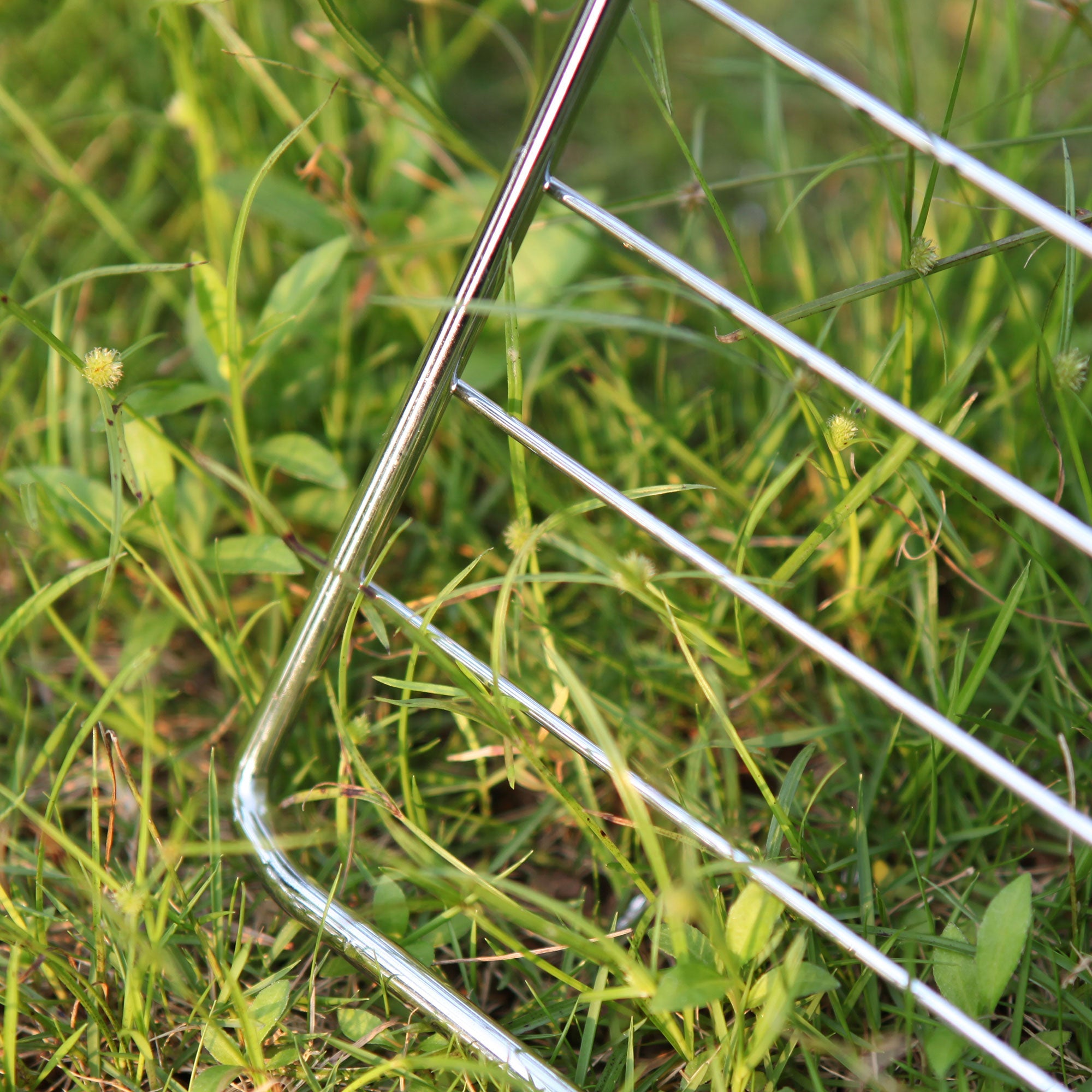 Close-up image of the Empava 24 Inch Wall Oven Rack corner resting on green grass. The shiny, reflective surface of the rack contrasts with the various shades of green in the grass, which include some small plants and blades.