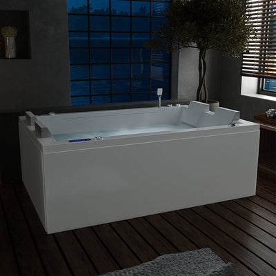 A modern bathroom features the 71 in. Freestanding Combination Massage 2-Person LED Tub With Center Drain by Empava, filled with water and perfect for indulging in Revi-Skin Therapy. Soft illumination enhances its sleek white surface. The room has dark tile flooring, a large window revealing a nighttime scene, and wooden blinds partially open.