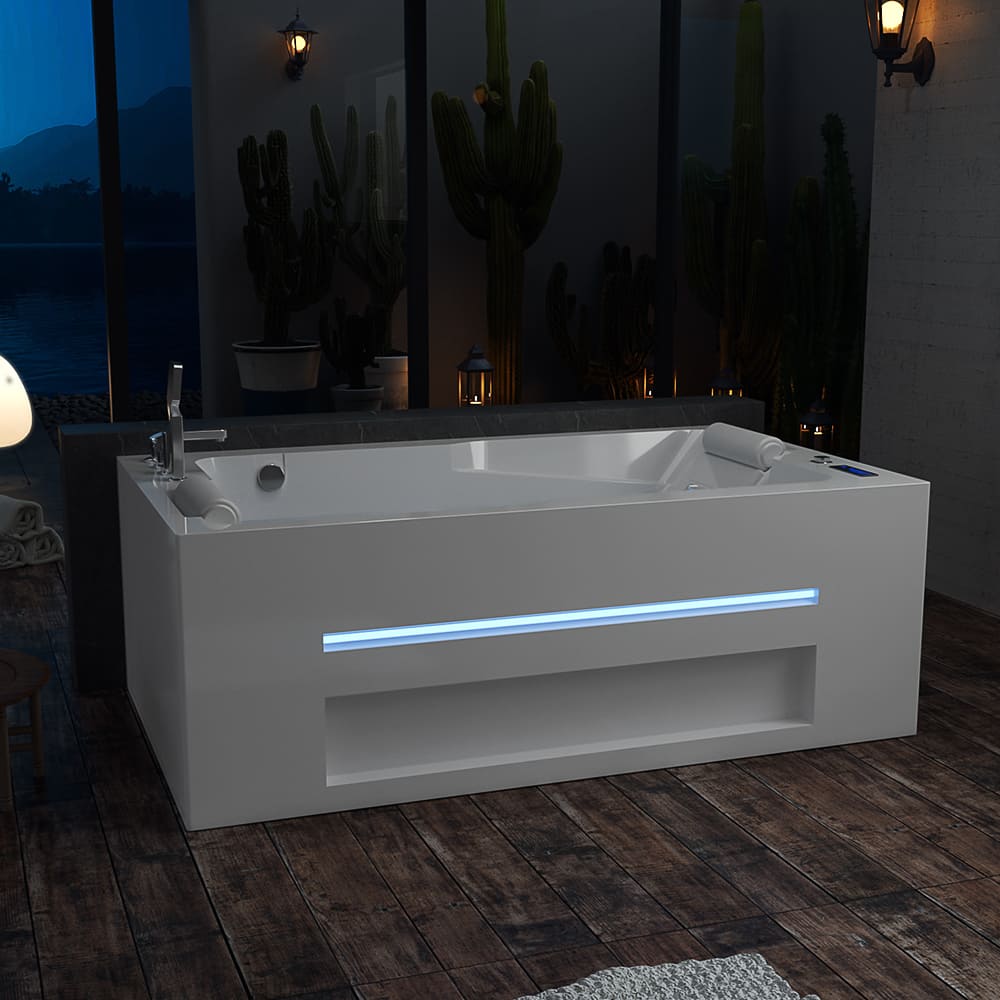 A modern 71-inch alcove massage thermostatic two-person LED tub with a right drain from Empava rests on a wooden floor. This rectangular white bathtub features a sleek design, built-in LED lighting, and an inline heater. The setting includes large windows revealing cactus plants outside and soft, warm lighting from wall sconces, creating a calm and inviting atmosphere.