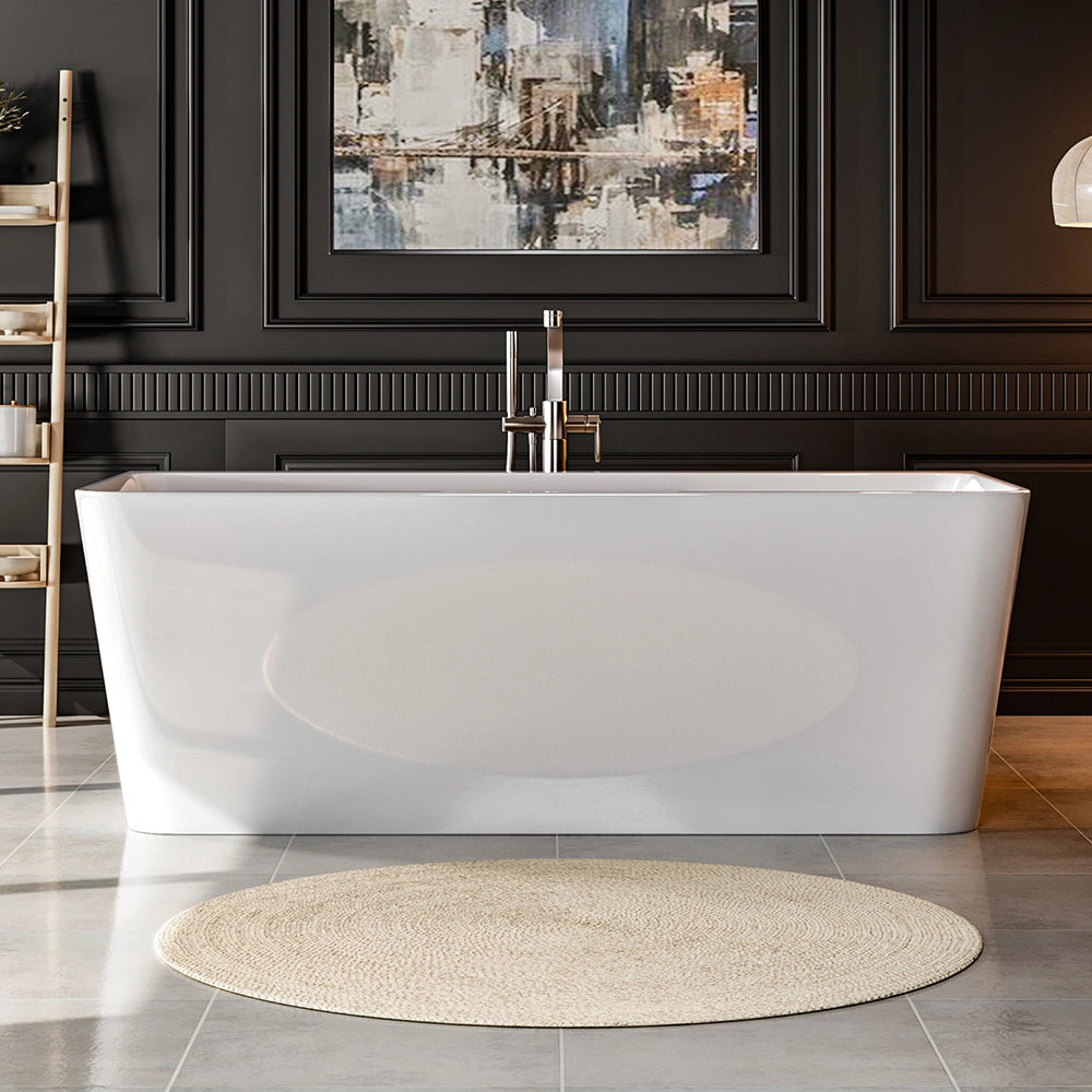 A modern bathroom featuring an ergonomic 67" Freestanding Soaking Tub with Center Drain made of acrylic material on a grey tiled floor. A round beige rug lies in front of the tub. The wall behind the tub is painted black with molding details and is adorned with a large framed abstract cityscape painting.