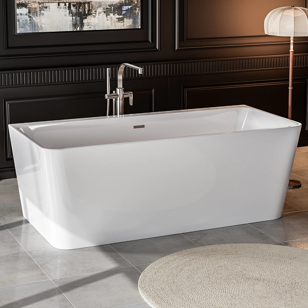 A modern bathroom featuring the 67" Freestanding Soaking Tub with Center Drain, an ergonomic white freestanding bathtub crafted from acrylic material with curved edges and a squared design. The room boasts dark paneled walls, light gray tiled flooring, a floor lamp with a round shade, and a circular beige mat in front of the tub.