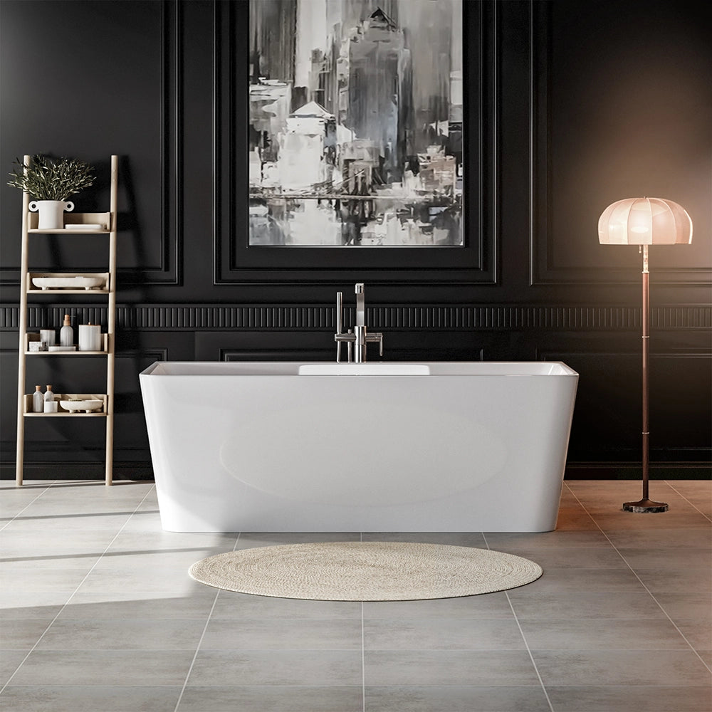 A modern bathroom showcases the 67" Freestanding Soaking Tub with Center Drain, an ergonomic white acrylic bathtub, set against a black paneled wall. Above the tub hangs an abstract cityscape painting. To the left, a wooden ladder shelf displays decor items, while to the right stands a floor lamp with a round shade. A beige rug lies in front of the tub.