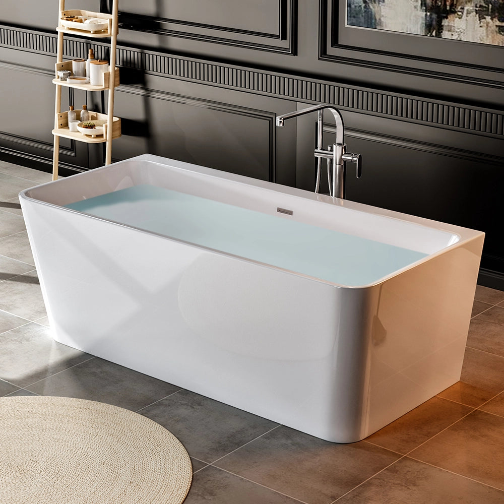 A modern bathroom showcasing a 67" Freestanding Soaking Tub with Center Drain, crafted from sleek acrylic material and filled with water. The room boasts dark paneled walls and gray tiled floors. In the background, there is a light wooden shelving unit stocked with toiletries. A round beige rug is partially visible on the floor.