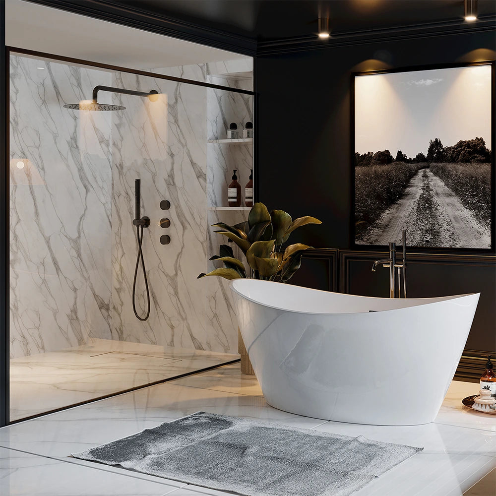 A modern bathroom showcases the 67" Freestanding Soaking Tub with Center Drain, a lightweight, freestanding white bathtub positioned prominently in the foreground alongside a sleek floor-mounted faucet. In the backdrop, there is a glass-enclosed shower equipped with a luxurious rainfall showerhead and elegant marble walls. The space is further enhanced by a large black and white landscape photograph and a potted plant.