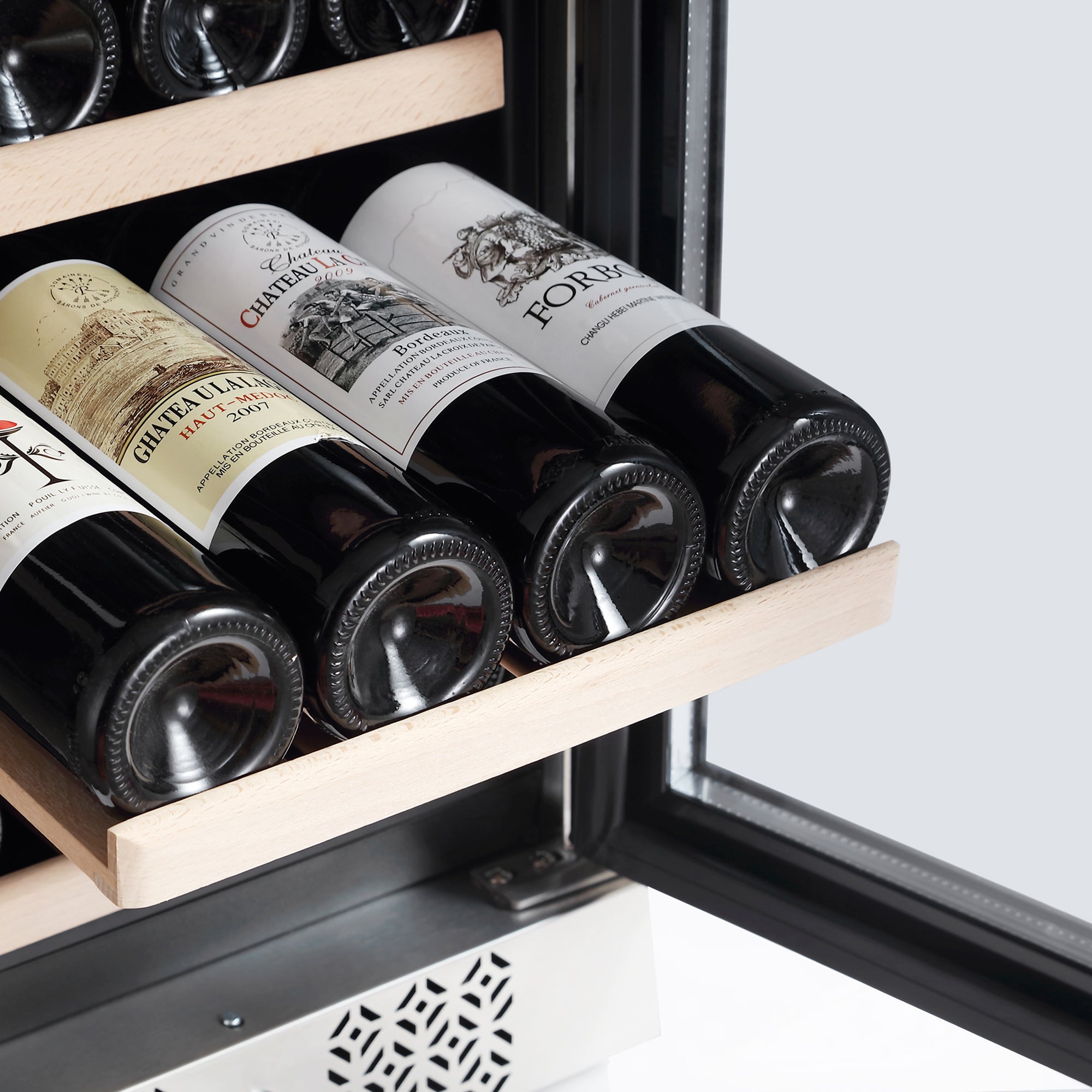 An Empava 15 Inch Dual Zone Small Wine Fridge with pull-out wooden shelves can hold four beautifully labeled bottles of wine. Stored horizontally, the bottles are elegantly showcased as the slightly open door reveals more wine treasures in the background.