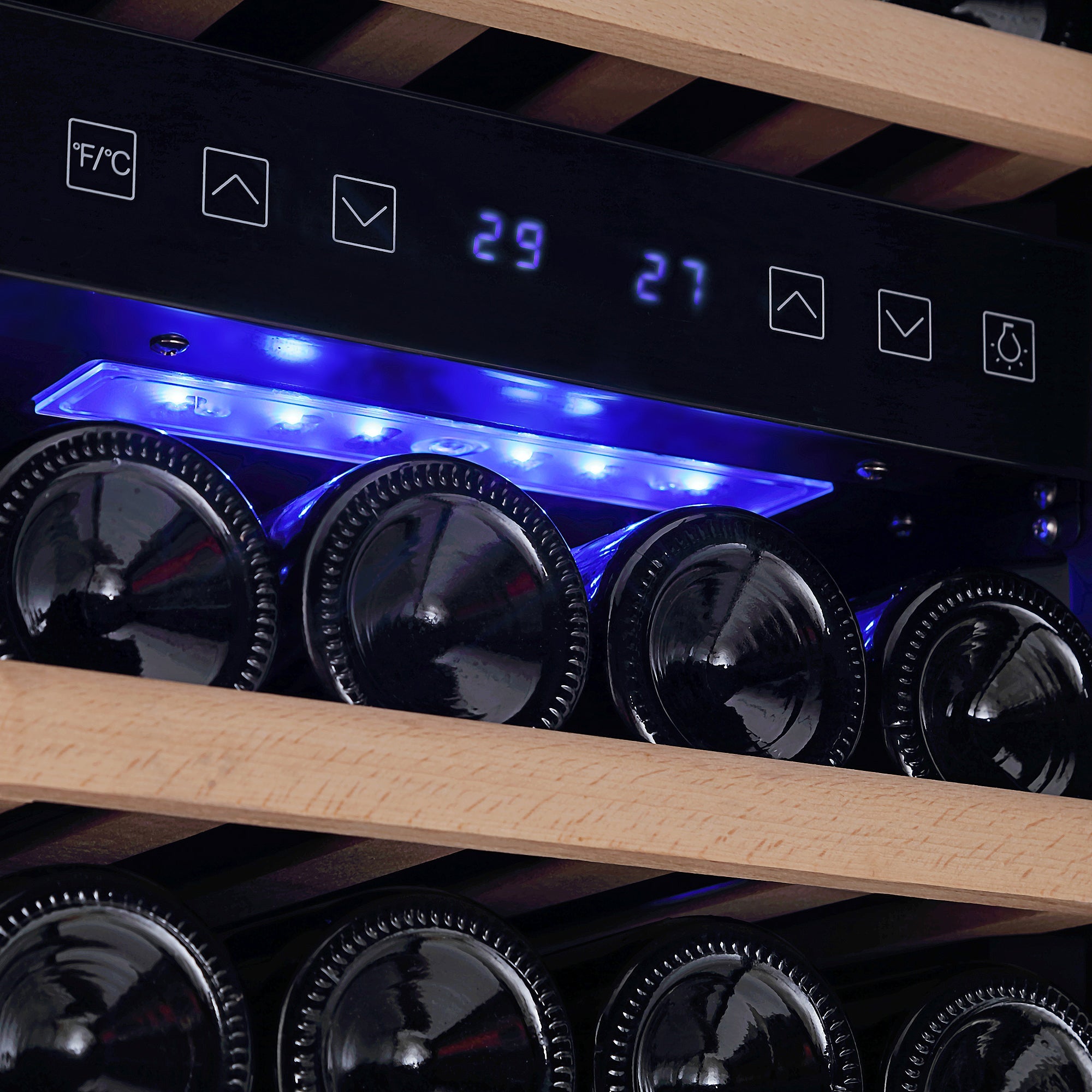 Close-up view of the Empava 15 Inch Dual Zone Small Wine Fridge's interior, showcasing two wooden shelves cradling lying wine bottles. The digital temperature display reads 29 and 27 degrees with buttons above for temperature control in Fahrenheit/Celsius, light settings, and other functions.