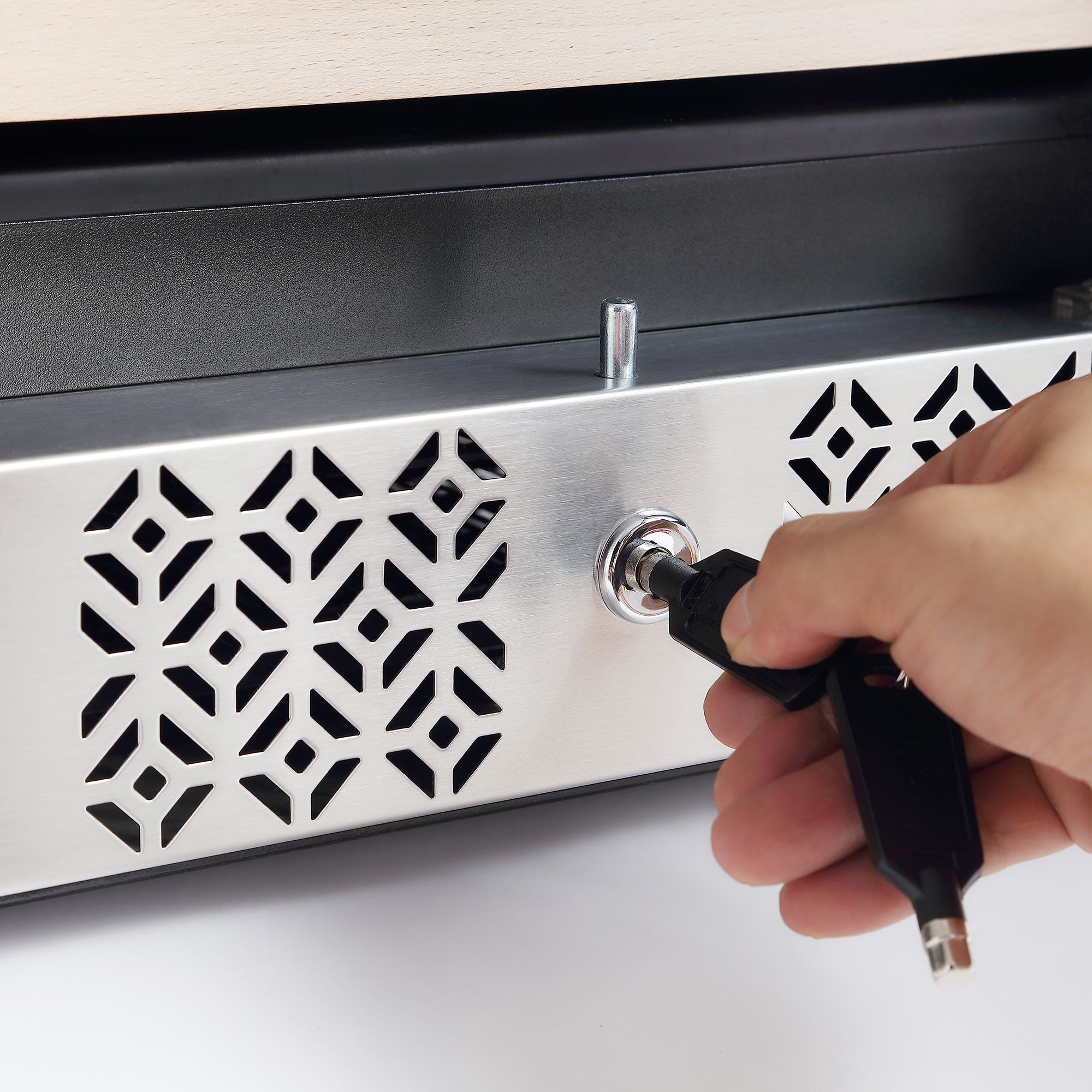 A hand is seen inserting a key into the lock positioned at the bottom edge of a metallic plate with a geometric diamond-shaped pattern, reminiscent of the sleek design found in the Empava 15 Inch Dual Zone Small Wine Fridge. The background is slightly blurred.