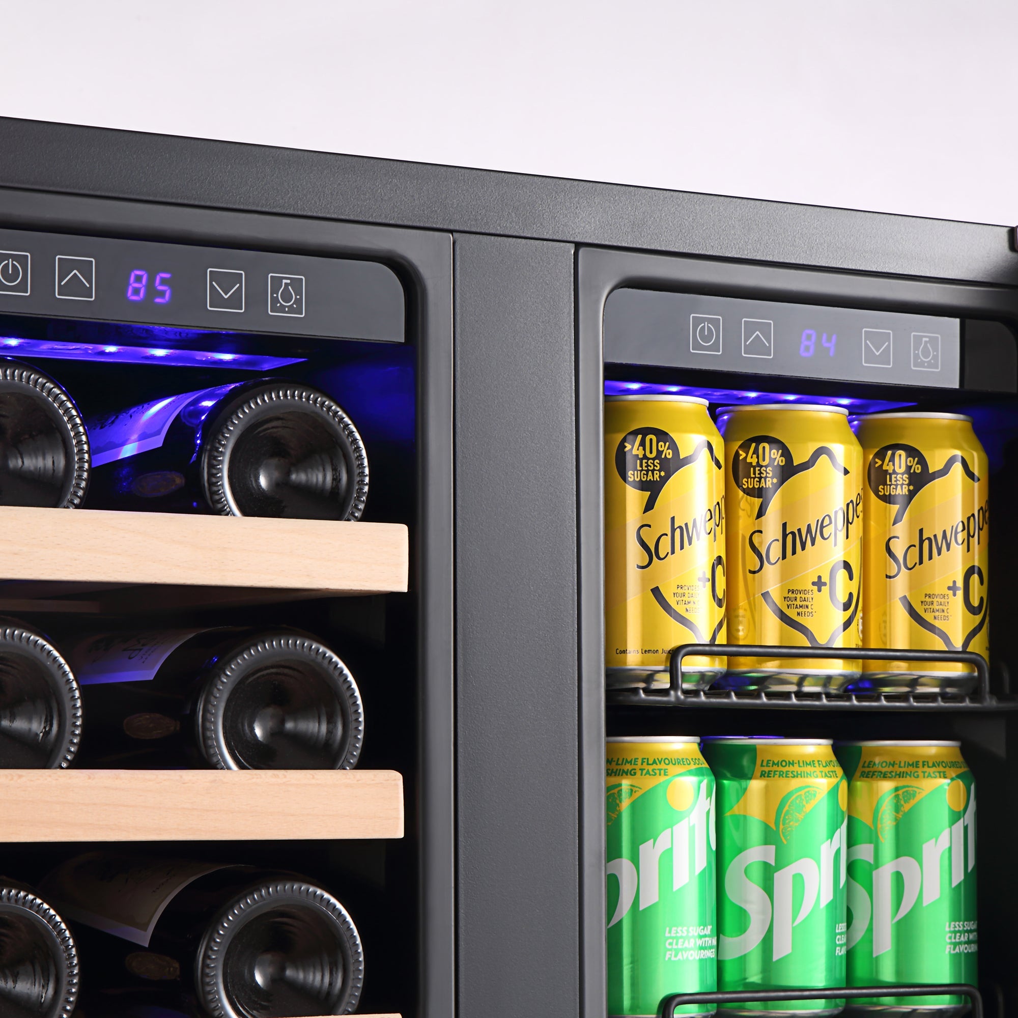 A close-up of an Empava 24" Dual Zone Wine and Beer Fridge Beverage Cooler displaying two sections. The left section holds several bottles of wine on wooden shelves, while the right section contains cans of Schweppes and Sprite. The temperature display shows 85°F on the left and 84°F on the right.