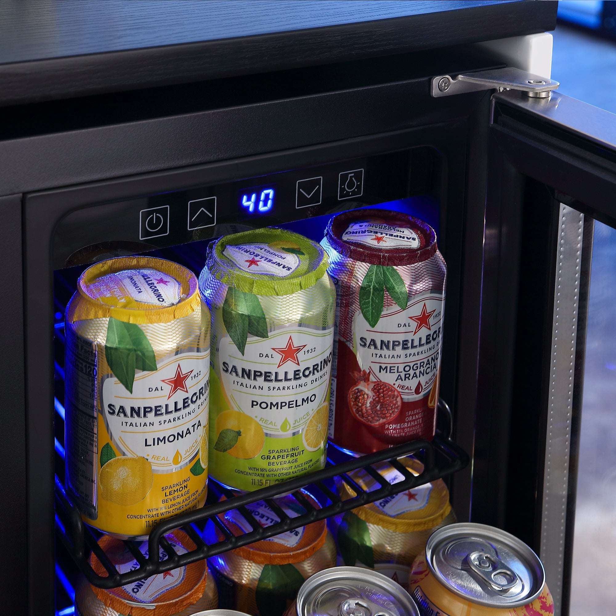 A sleek Empava 24" Dual Zone Wine and Beer Fridge Beverage Cooler houses a collection of San Pellegrino sparkling drinks, with varieties like Limonata, Pompelmo, and Melograno e Arancia. The digital temperature display reads "4.0," while additional beverage cans rest neatly on the lower shelf.