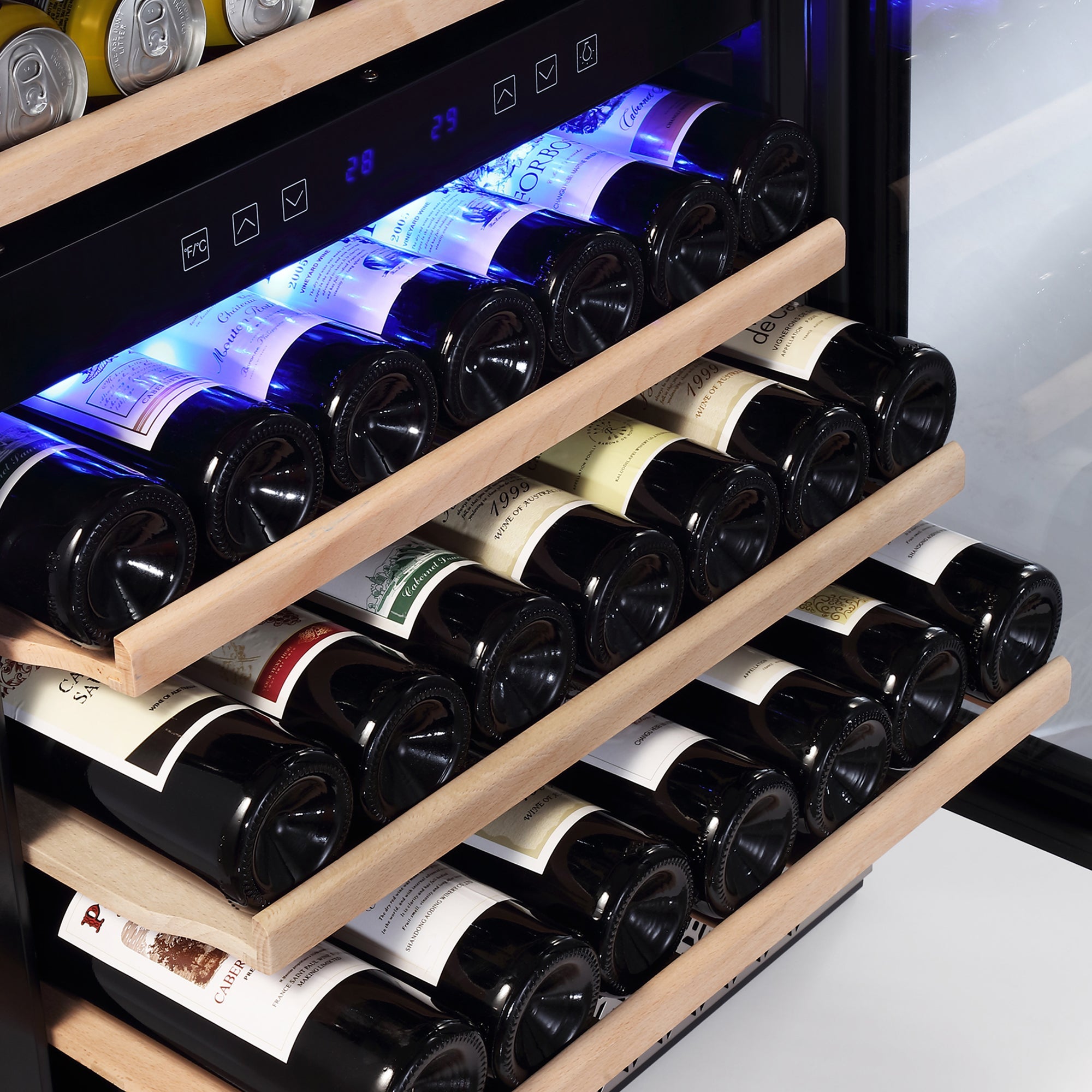 A close-up view of the Empava 24 Inch Dual Zone Wine & Beverage Cooler reveals several wooden shelves, each holding multiple horizontally-placed wine bottles. The partially pulled-out shelves showcase the bottle labels, illuminated by a blue interior light.