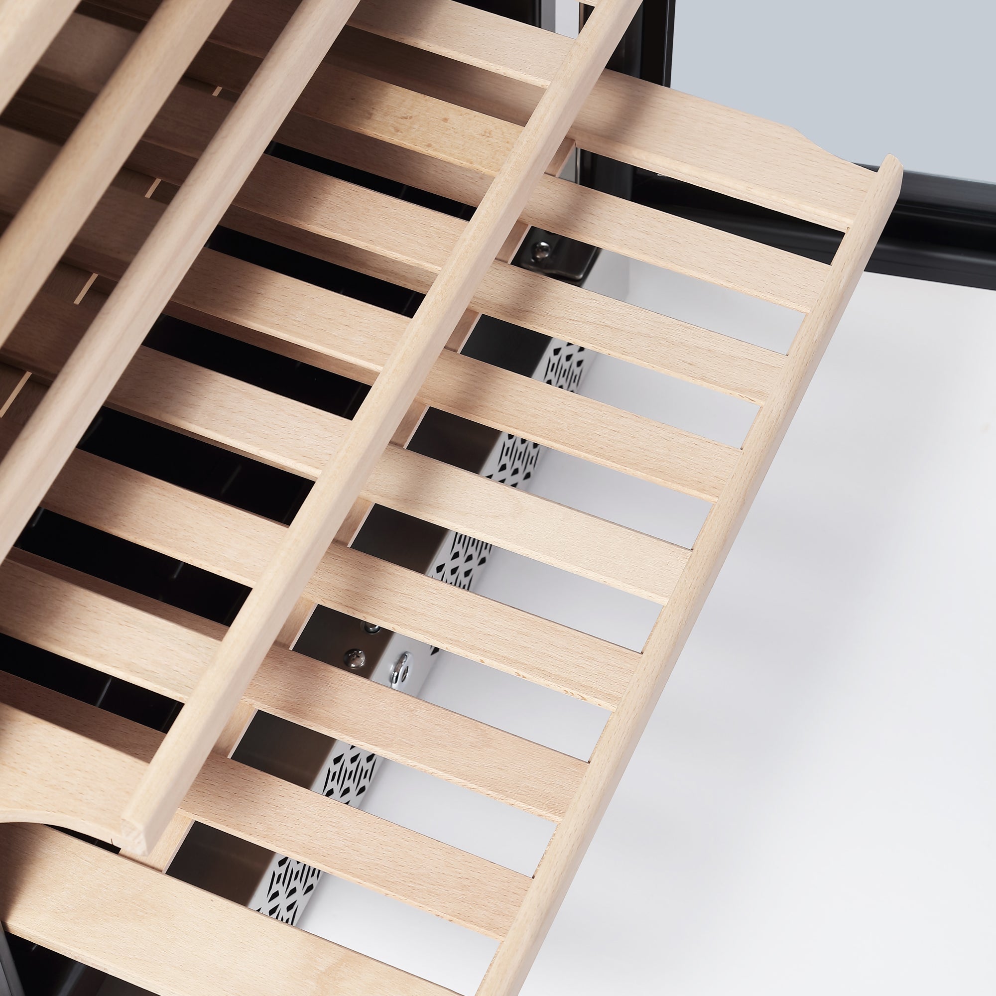 A close-up view of a wooden slatted shelf from the Empava 24 Inch Wine Cooler Wine Fridge, which holds up to 52 bottles, shows light-colored wood with evenly spaced horizontal slats. The slatted shelf is partially extended, revealing a metallic grille underneath. The background is a neutral light gray.