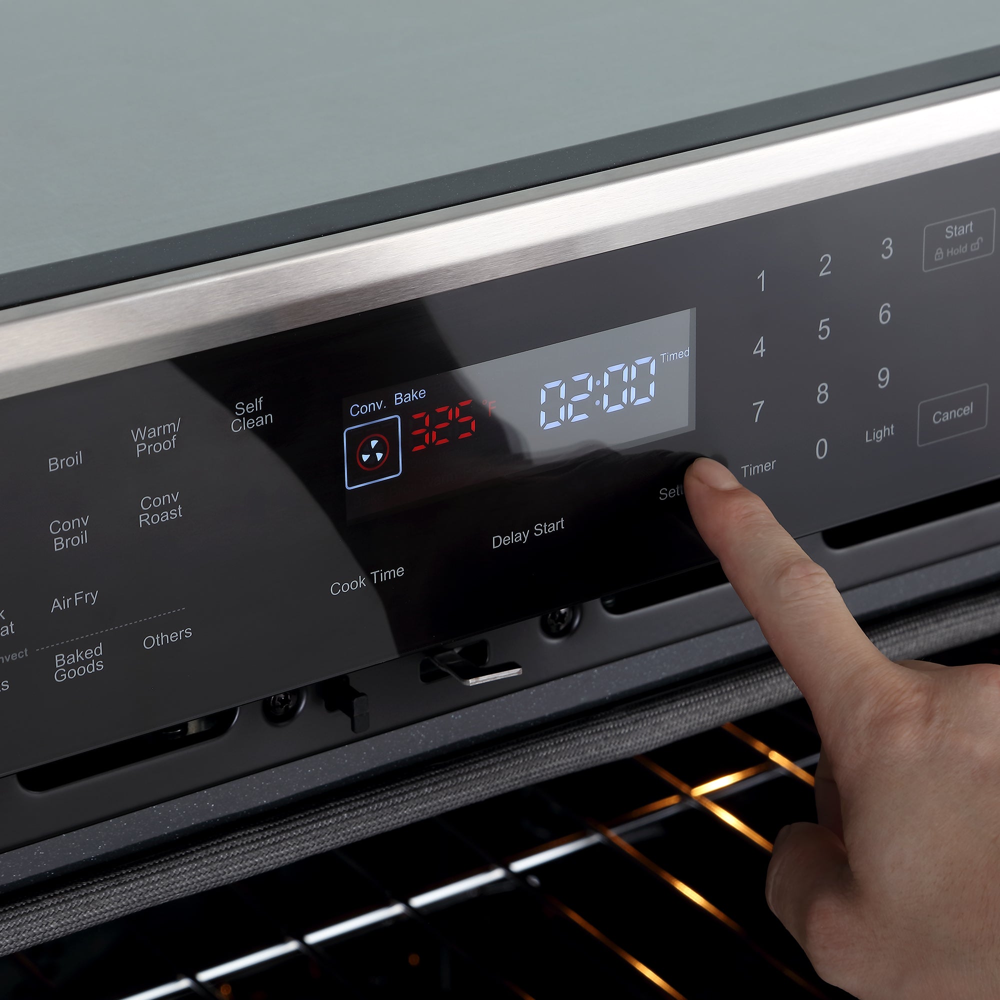 A close-up of a finger pressing buttons on the control panel of the Empava 30" Electric Single Wall Oven with its 4-layer glass door. The display shows the oven is set to "Conv. Bake" mode at 325°F with a timer of 2 hours and 20 minutes. The oven door is slightly open, revealing the inside.