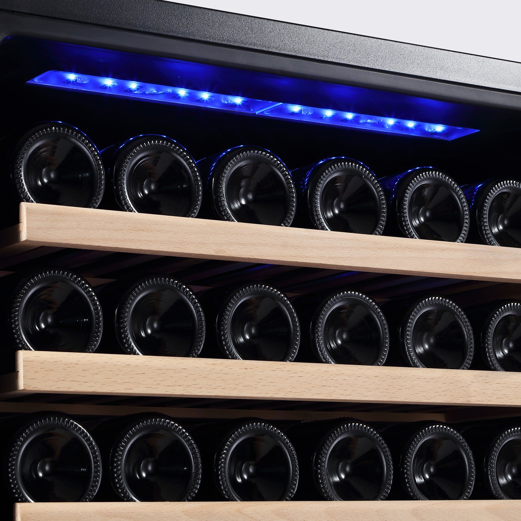 A close-up view of wine bottles stored on wooden racks within the Empava 55" Tall Dual Zone 100 Bottle Wine Fridge. The refrigerator features a black interior and blue LED lighting at the top, illuminating the horizontally arranged bottles. Its dual zones ensure optimal storage conditions, reducing the risk of wine oxidization.