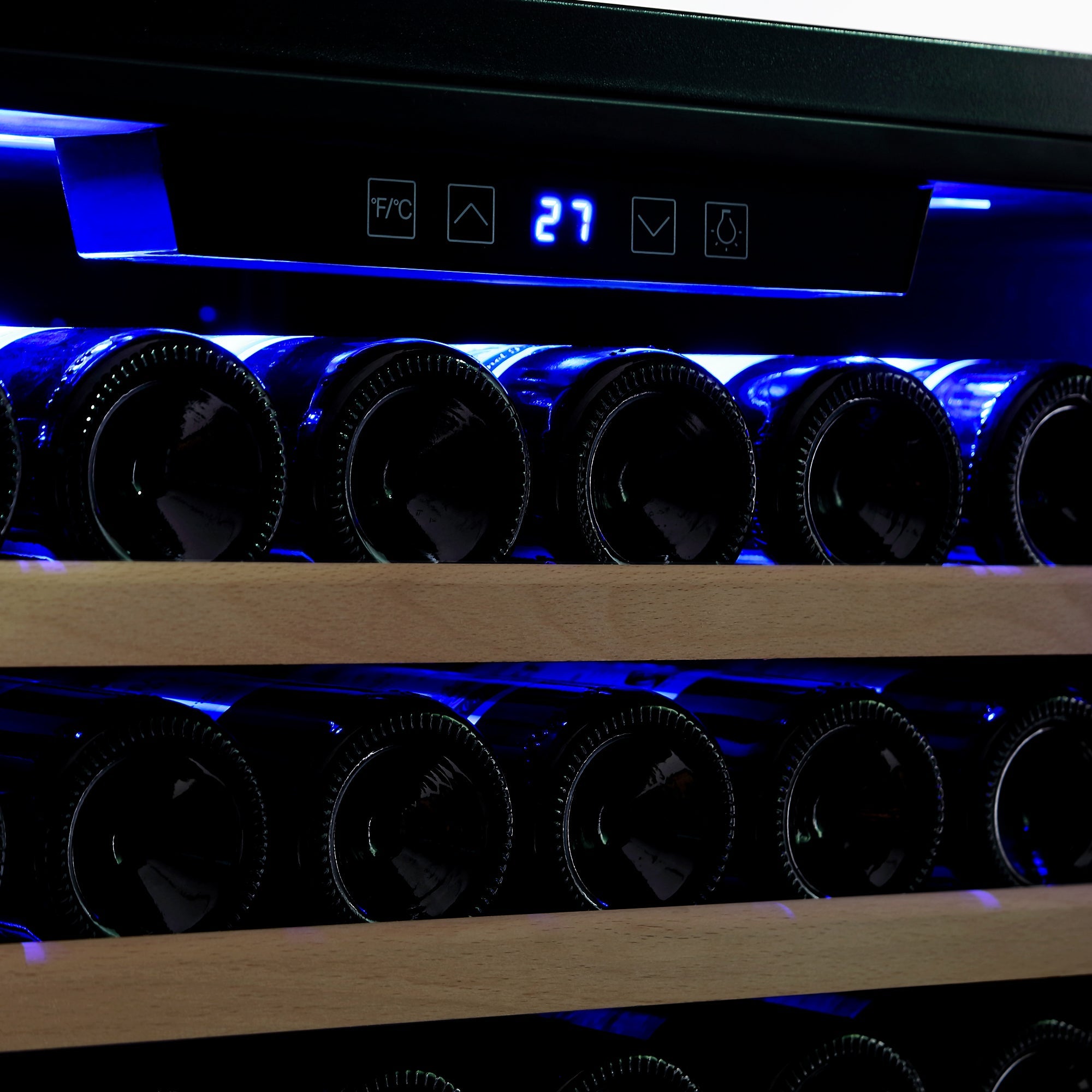 A close-up of wine bottles stored on horizontal wooden racks inside the Empava Wine Cooler 70" Tall Wine Fridge with an enormous capacity. The temperature display on the upper part of the fridge door shows "27" degrees Celsius, illuminated by a blue LED light.