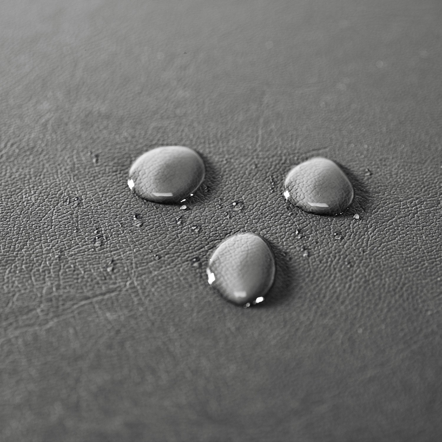 Close-up of three water droplets on a textured, dark gray surface of the Outdoor Hot Tub Cover for Empava SPA3527. The droplets are arranged in a loose triangular pattern, highlighting the contrast between the smooth water and the rough texture of the background.