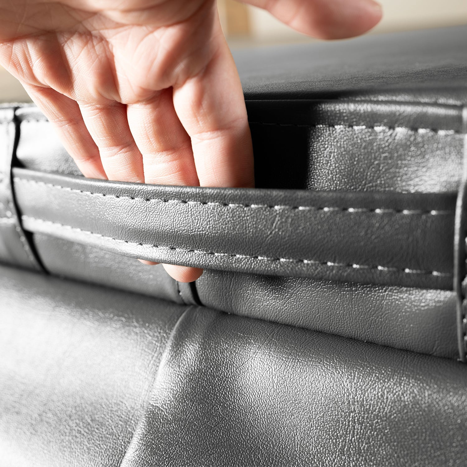 Close-up of a hand lifting the handle on the Outdoor Hot Tub Cover for Empava SPA3550, revealing a storage compartment underneath. The grey cover features visible stitching, and the material appears to be leather or a leather-like fabric.