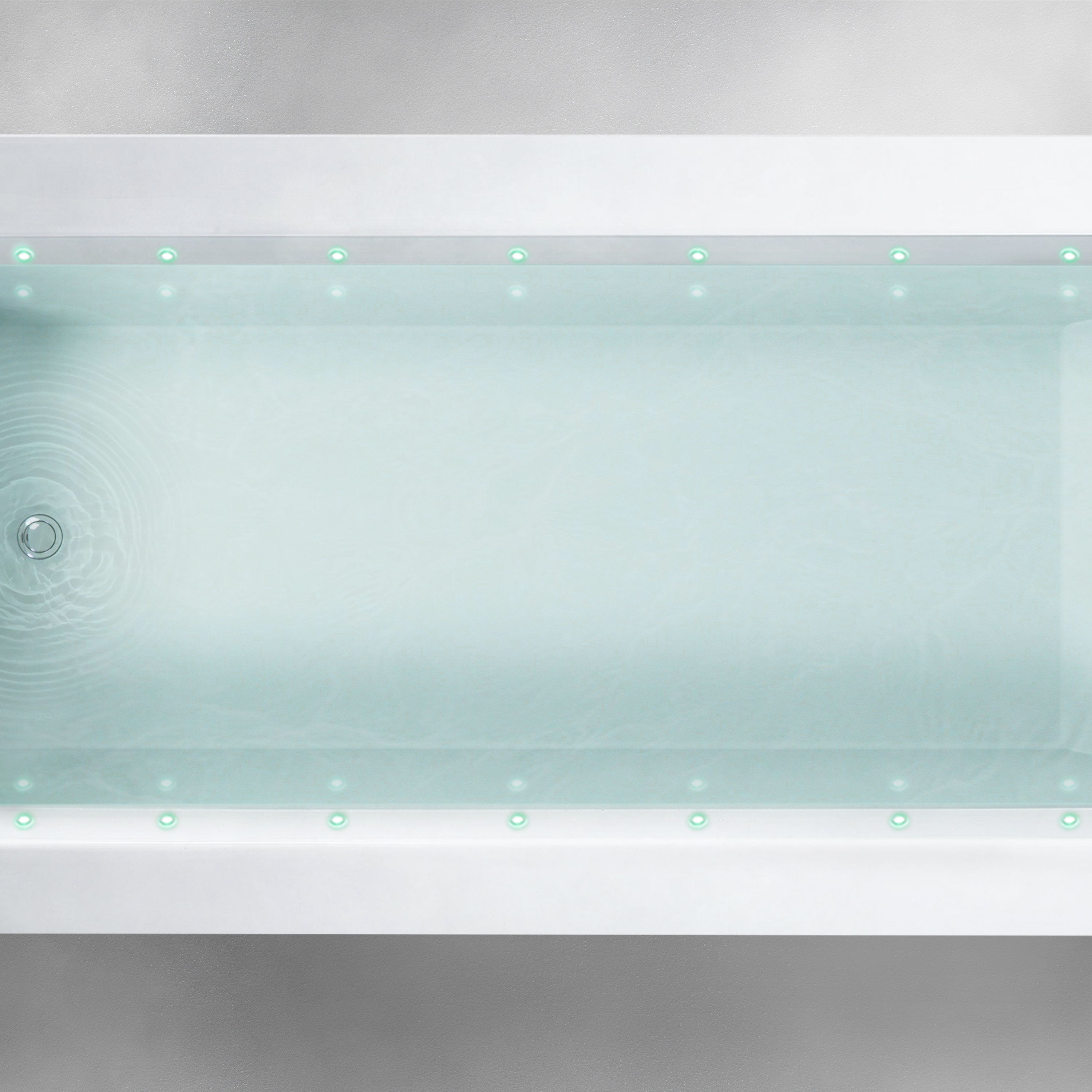 Top view of a rectangular Custom Function bathtub filled with clear water. Small green LED lights line the inner rim, evenly spaced along the length and width of the tub. The bathtub is set against a light gray, textured background.